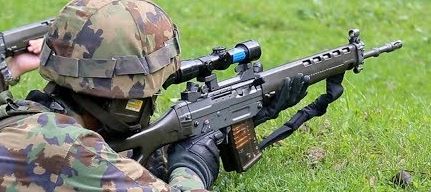 Schweizer Soldat mit Tarnkleidung im Liegen beim Zielen mit einem Sturmgewehr, optimierte Atemtechnik für Präzisionsschüsse.